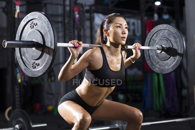 Chinese woman lifting barbell at gym — Stock Photo