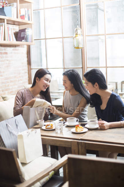 Chinese woman demonstrating new clothing to female friends in coffee shop — Stock Photo