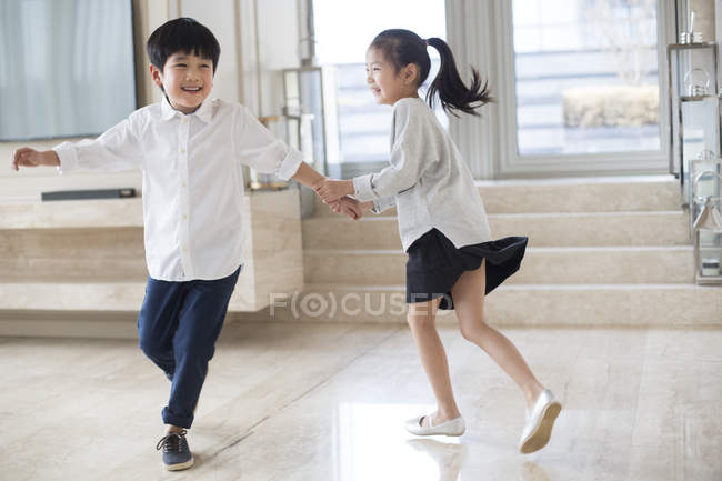 Irmãos chineses de mãos dadas e correndo na sala de estar — Fotografia de Stock