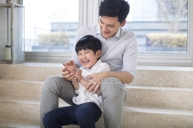 Chinese father tickling son in living room — Stock Photo