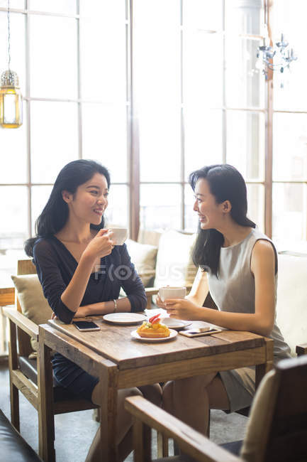 Chinese female friends drinking coffee and talking in cafe — Stock Photo