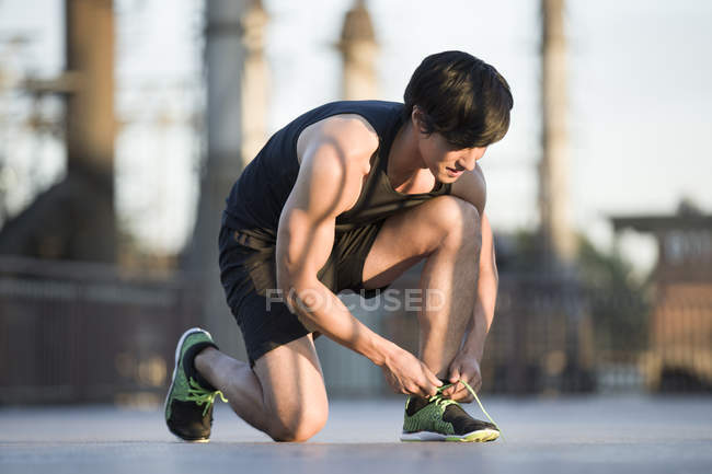 Asian jogger tying shoelaces on street — Stock Photo