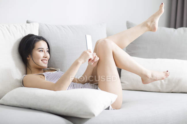 Asiatin benutzt Smartphone auf Sofa im Hausinneren — Stockfoto