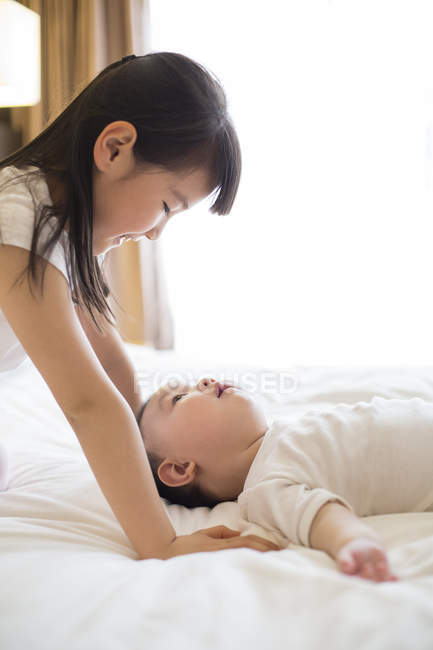 Chinese girl playing with baby boy on bed — Stock Photo