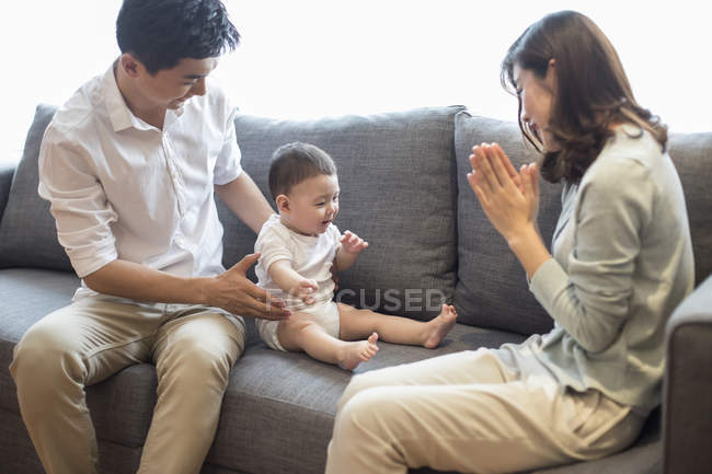 Madre china aplaudiendo mientras mira sentado bebé niño - foto de stock