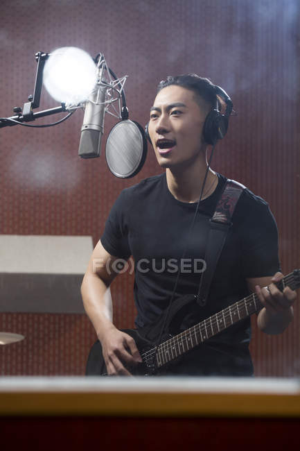 Hombre chino cantando con guitarra en estudio de grabación - foto de stock