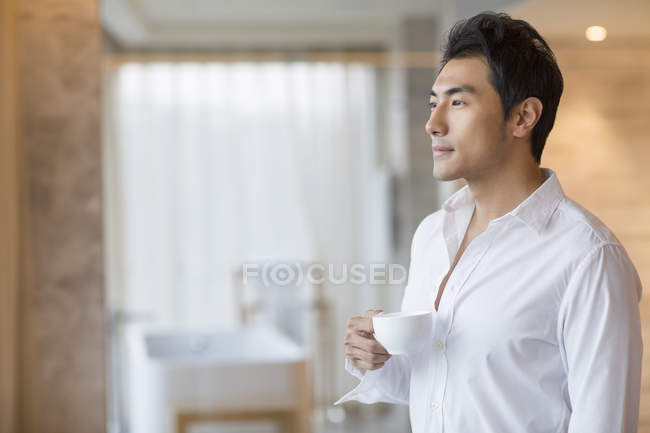 Homem chinês segurando xícara de café em casa — Fotografia de Stock