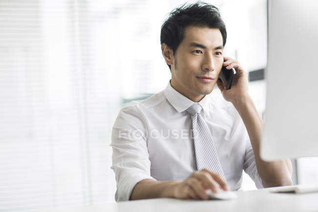 Chinese businessman talking on phone at desk in office — Stock Photo