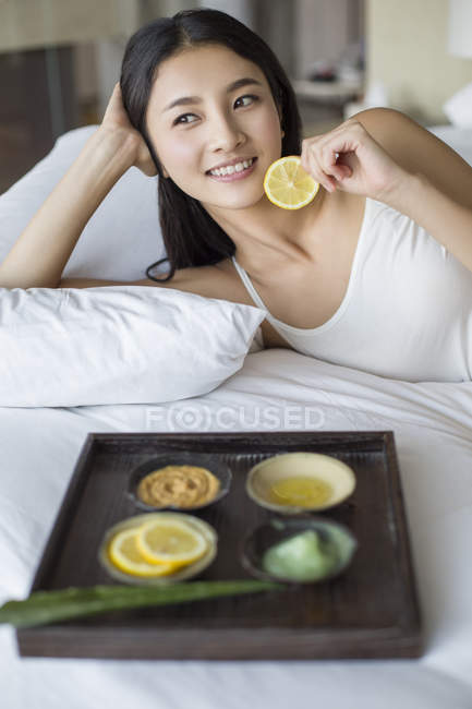 Chinese woman lying on bed with tray of natural facial mask ingredients — Stock Photo