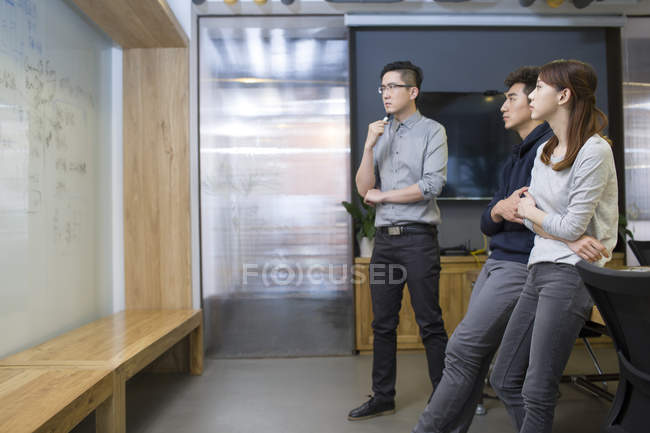 Chinese office workers looking at whiteboard in board room — Stock Photo