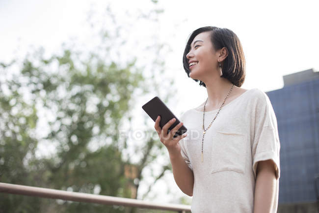 Chinese woman holding smartphone in city — Stock Photo