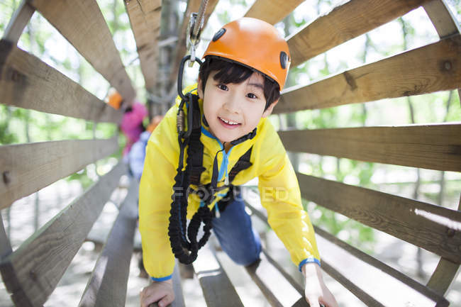 Chinese boy in tree top adventure park wooden tube — Stock Photo