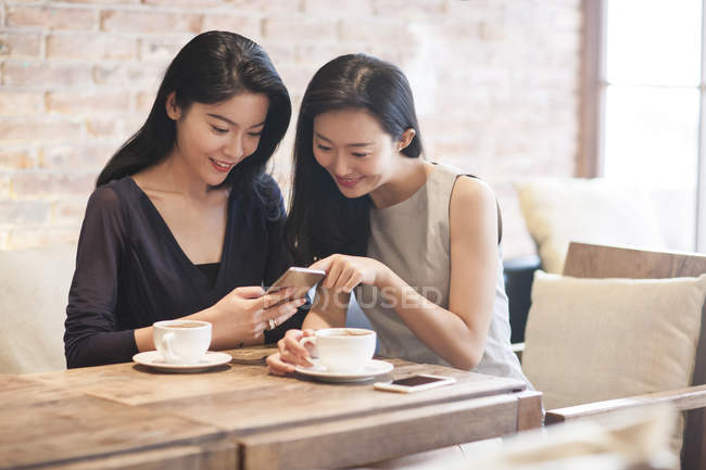 Amigos femeninos chinos usando teléfono inteligente en la cafetería - foto de stock