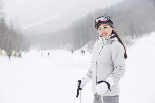 Esquiadora china de pie con bastones de esquí en la pista - foto de stock