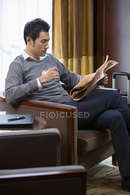 Chinesischer Geschäftsmann liest Zeitung im Hotelzimmer — Stockfoto