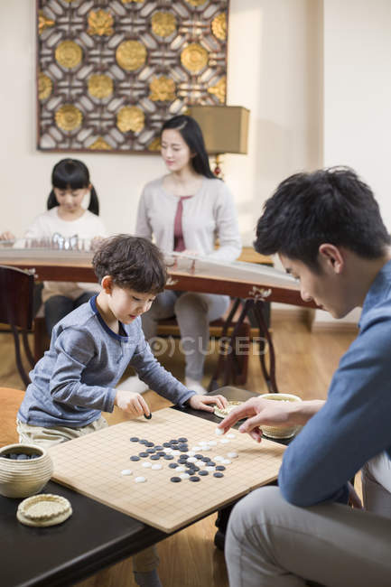 Actividades de ocio en familia asiática con Go game e instrumento musical - foto de stock