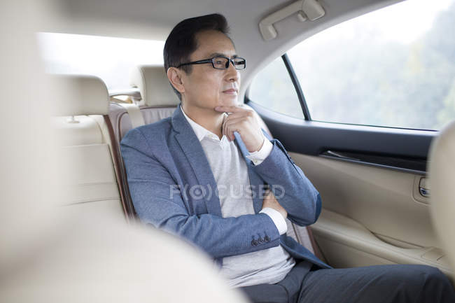 Asiatischer Mann sitzt auf der Rückbank des Autos und schaut durch das Fenster — Stockfoto