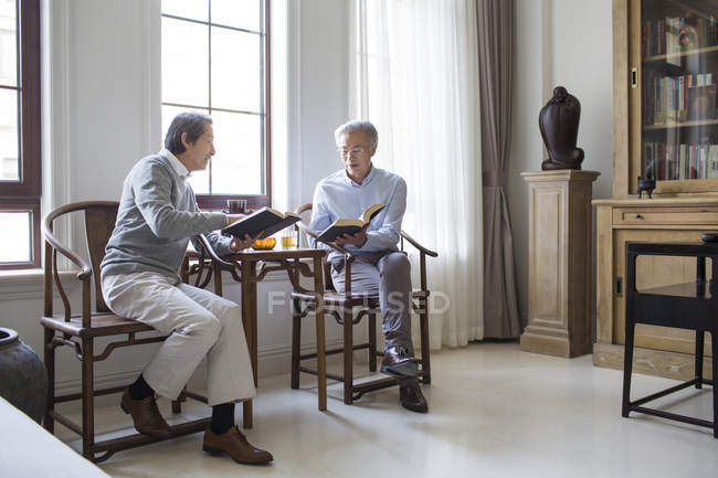 Chinesische Männer diskutieren beim Lesen von Büchern im Wohnzimmer — Stockfoto