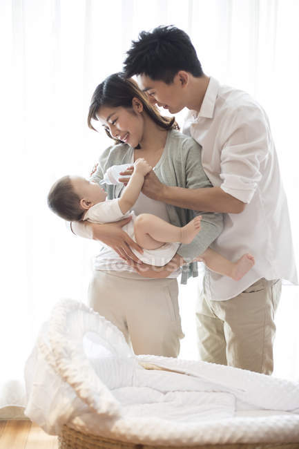 Pais chineses alimentando bebê menino no quarto com berço — Fotografia de Stock