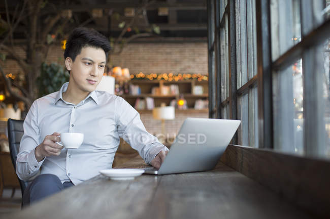 Homem chinês usando laptop no café com xícara de café — Fotografia de Stock