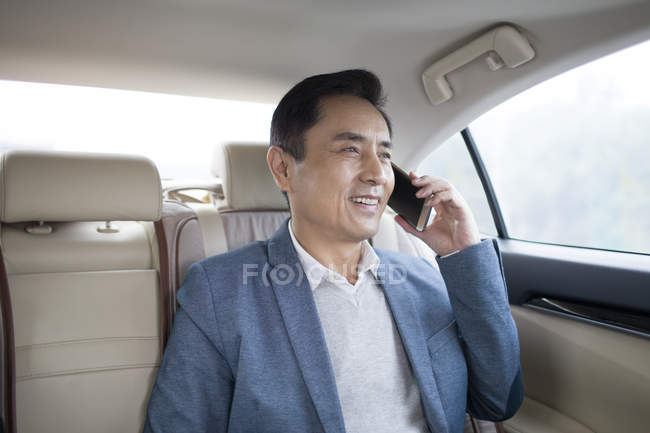 Asian man talking on phone on car back seat — Stock Photo