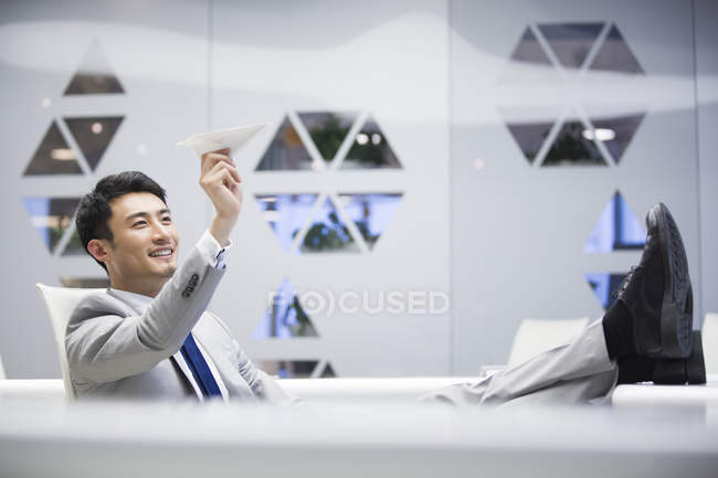 Young Chinese businessman flying paper airplane in office — Stock Photo