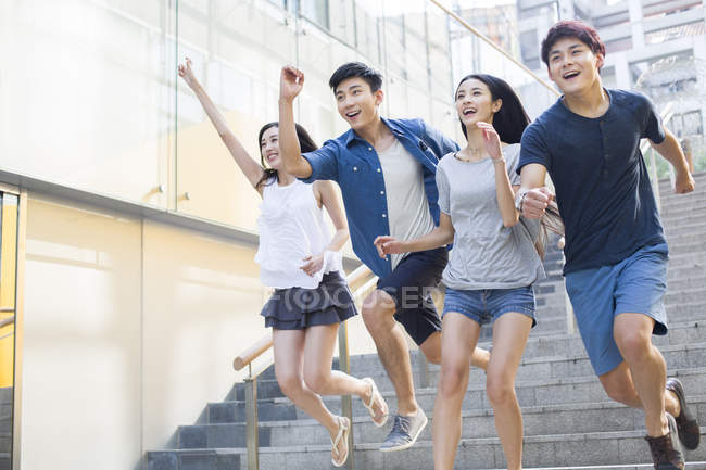 Chinese friends running down steps on street — Stock Photo