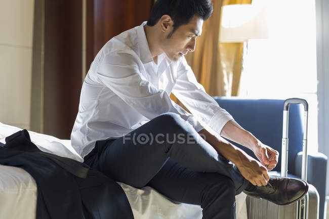 Hombre de negocios chino atando zapatos en la habitación de hotel - foto de stock