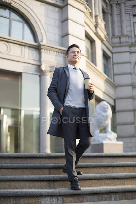 Uomo d'affari cinese a piedi giù per la costruzione di gradini con caffè in città — Foto stock