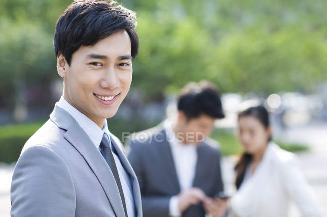 Chinese businessman standing on street with co-workers in background — Stock Photo