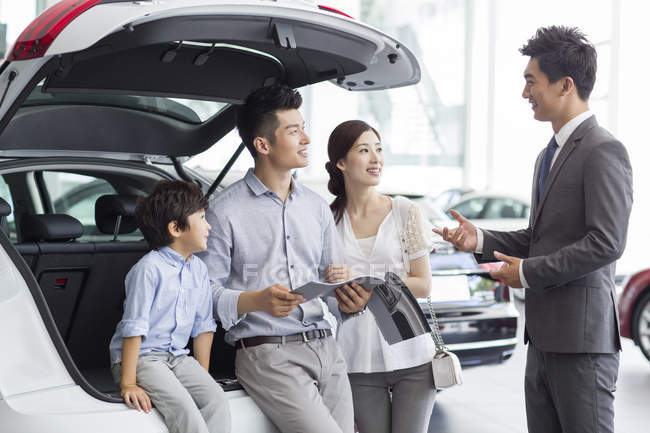 Chinese family sitting in car trunk in showroom with car seller — Stock Photo