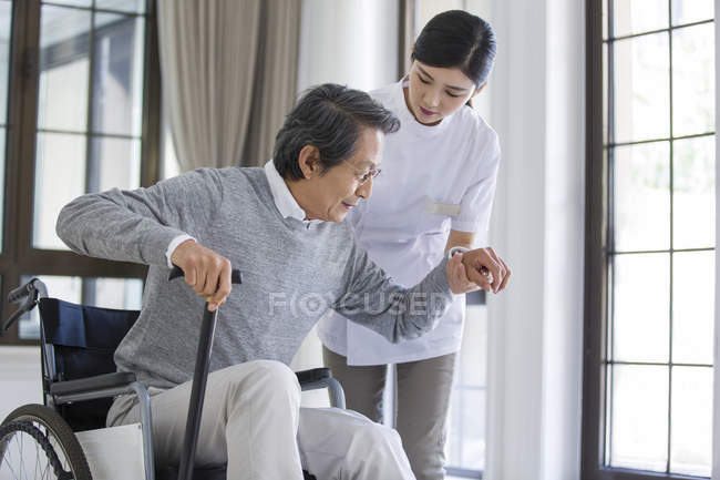 Chinese nursing assistant taking care of senior man in wheelchair — Stock Photo