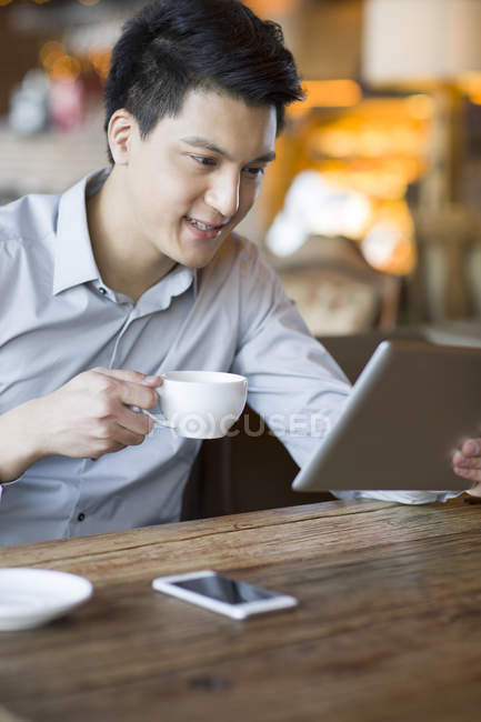 Chinese man using digital tablet and holding cup in cafe — Stock Photo