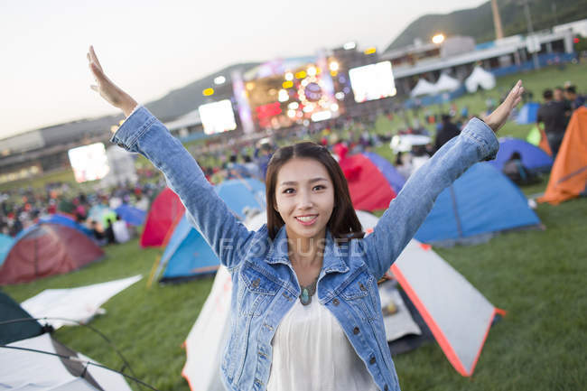 Китаянка с поднятыми руками позирует с фестивальным кемпингом на заднем плане — стоковое фото