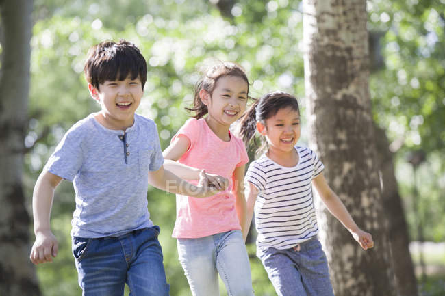 Chinese children holding hands and running in woods — Stock Photo