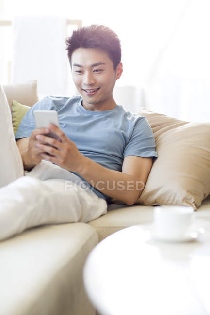 Homem chinês usando smartphone no sofá — Fotografia de Stock