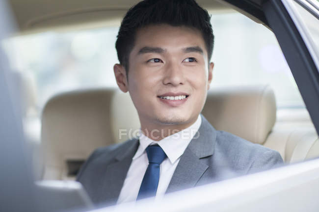 Chinese businessman sitting on car back seat and looking through window — Stock Photo