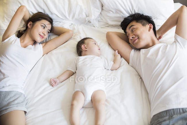 Familia china con bebé niño acostado en la cama - foto de stock