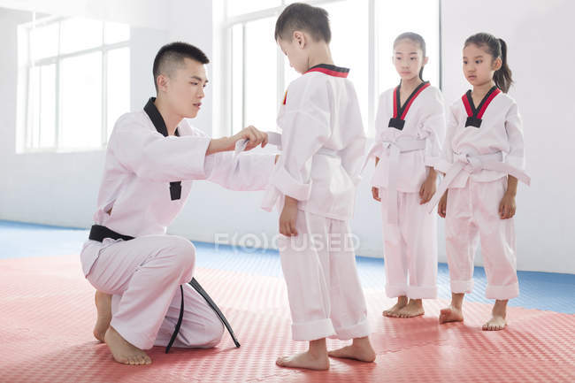 Instrutor chinês amarrando estudantes taekwondo cintos — Fotografia de Stock