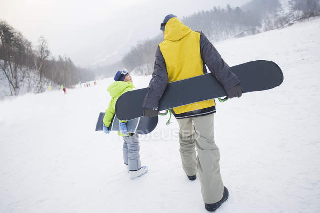 Padre e hijo caminando con tablas de snowboard sobre nieve - foto de stock