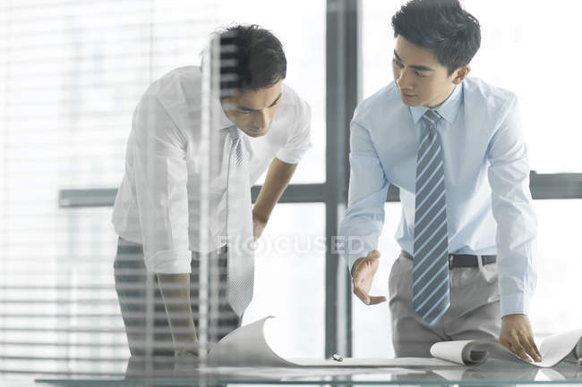 Chinese businessmen discussing blueprint at desk in office — Stock Photo