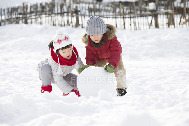Chinese children rolling snowball outdoors — Stock Photo
