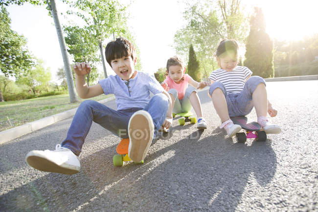 Chinese children sitting while riding on skateboards — Stock Photo