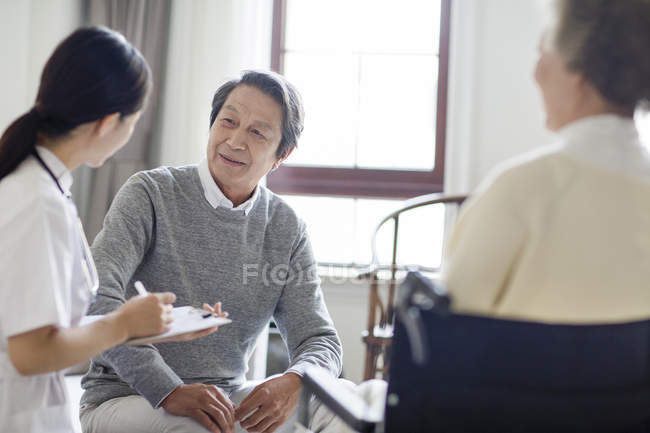 Chinese nurse talking with senior man and writing down in clipboard — Stock Photo
