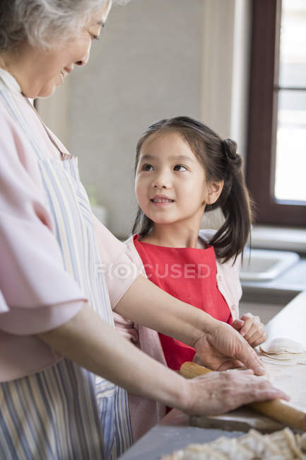 Chinese granddaughter and grandmother making dumplings in kitchen — Stock Photo