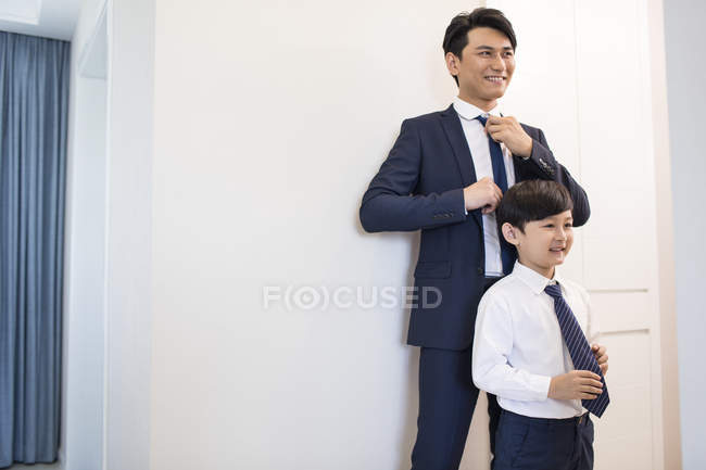 Padre e hijo chinos ajustando lazos en la mañana - foto de stock