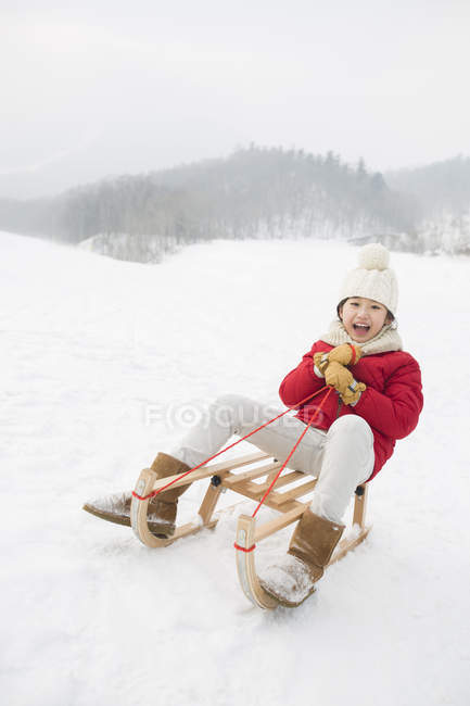 Chinese girl sliding on sled in snowy weather — Stock Photo