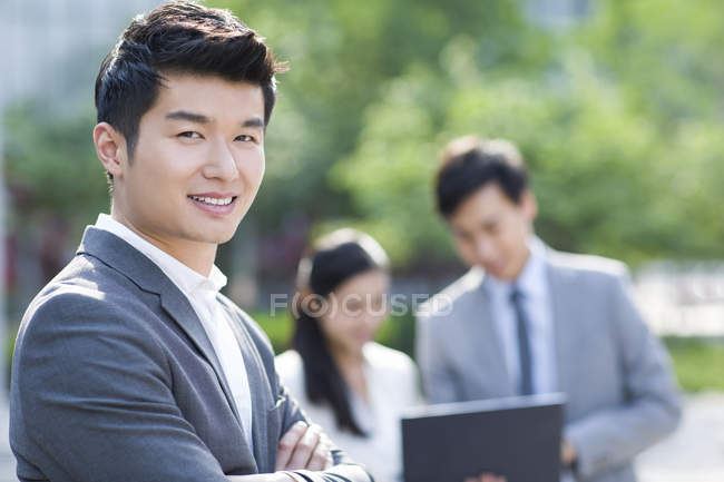 Китайський бізнесмен, стоячи на вулиці з колегами у фоновому режимі — стокове фото