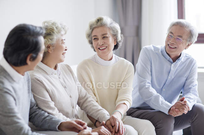 Amis chinois aînés parlant sur le canapé dans le salon — Photo de stock