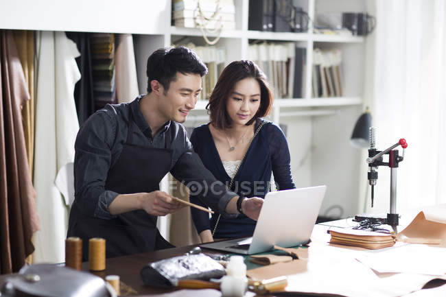 Artesano asiático y cliente en estudio con portátil - foto de stock